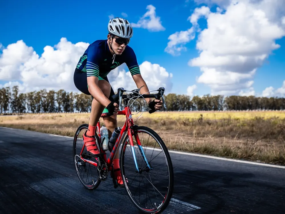 A cyclist riding a prepared road bike on an open road under a bright sky.