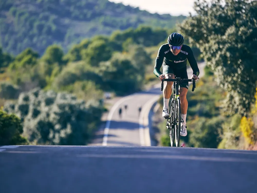 A cyclist climbing a winding road through the green hills inland from the coast.