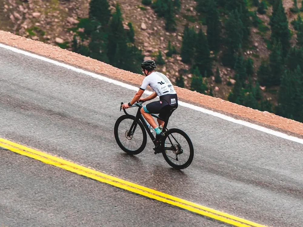 A cyclist on a quiet mountain road lined with pine forest on a clear morning.